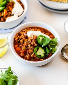 two bowls of chili with sour cream on top and lime slices around the rims