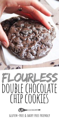 a chocolate cookie is being held up by someone's hand with the words flourless double chocolate chip cookies