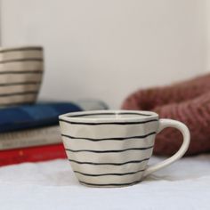 a white coffee cup sitting on top of a table next to books and a blanket