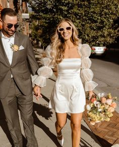 a man and woman are walking down the street holding hands while dressed in white dresses