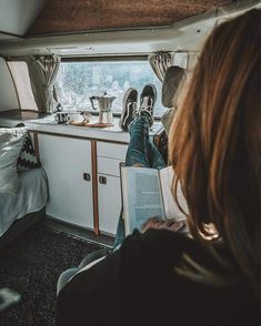 a woman reading a book while sitting in a camper with her feet up on the kitchen counter