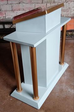 a white and gold church pulpit with two columns on each side, in front of a brick wall