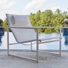 a white lounge chair sitting next to a swimming pool with trees in the back ground