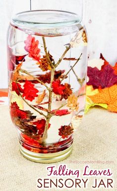 a glass jar filled with leaves on top of a table next to a pile of autumn leaves