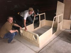 two men kneeling down next to a bed made out of plywood and wood planks