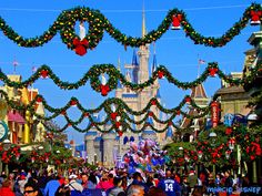 people are walking down the street in front of christmas decorations and castle at disney world