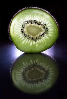 a kiwi cut in half sitting on top of a black table next to a mirror