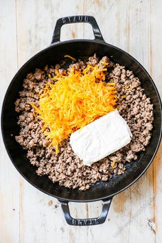 a skillet with cheese and ground beef in it on a wooden table next to a fork