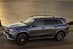 a silver mercedes gls driving down the road by the ocean at sunset or dawn