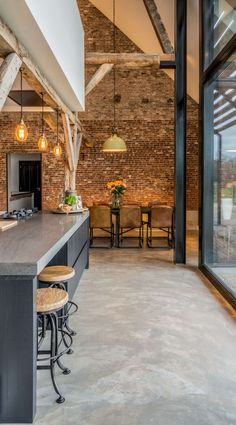 an open kitchen and dining area with exposed brick walls, floor to ceiling windows, and bar stools