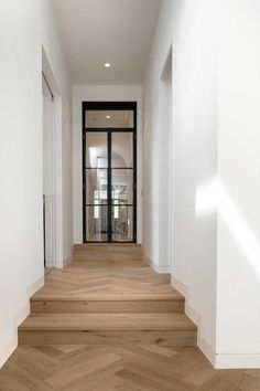 an empty hallway with wooden floors and white walls, leading to a glass door that leads to another room