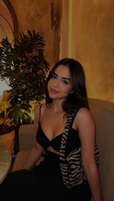 a woman sitting in a chair next to a potted plant and wearing a black dress