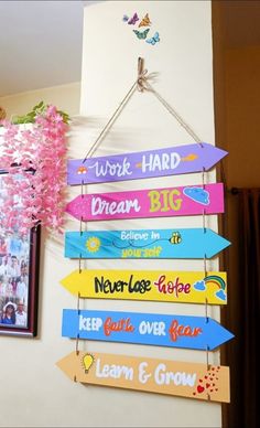 colorful wooden signs hanging on the wall in front of a pink flower and framed photo