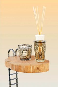 a wooden table topped with two glass cups filled with reeds next to a metal faucet