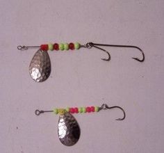 two metal spoons with beaded hooks hanging from them on a white wall background