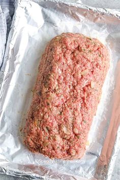 raw ground meat on aluminum foil with a wooden spoon next to it, ready to be cooked