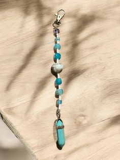 a blue beaded necklace is hanging from a chain on a wooden table next to a tree