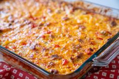 a casserole dish with cheese and meat in it on a red table cloth