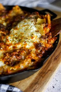 a skillet filled with cheesy pasta on top of a wooden cutting board