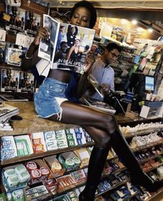 a woman sitting on top of a counter in a store holding up a magazine and looking at the camera