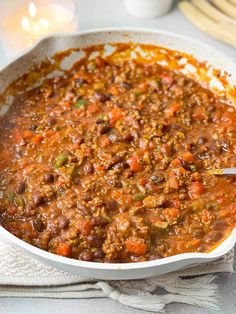 a white bowl filled with chili and meat on top of a table next to silverware