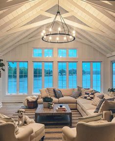 a living room filled with lots of furniture next to large windows and a chandelier hanging from the ceiling