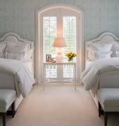 two white beds sitting next to each other in a bedroom under a window with shutters