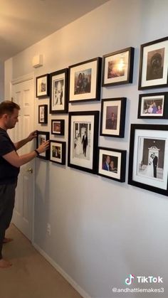 a man standing in front of a wall with pictures hanging on the side of it