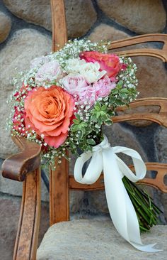 a bouquet of flowers sitting on top of a wooden chair next to a stone wall