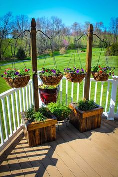 an outdoor deck with potted plants and hanging planters on the posts, along with two wooden boxes filled with flowers