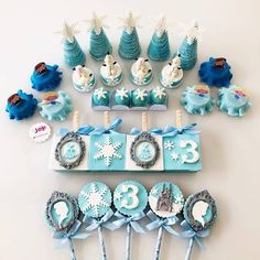 a table topped with cupcakes covered in frosting next to blue trees and snowflakes