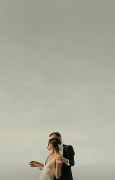 a bride and groom are standing on the beach with their arms outstretched to each other