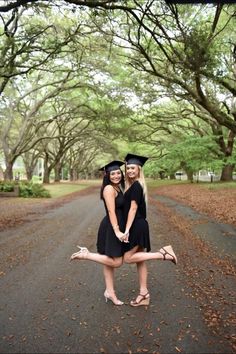 two young women in graduation gowns posing for a photo on the road with trees