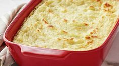 a red casserole dish with cheese in it on a white and gray cloth