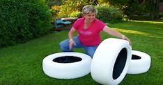 a woman kneeling down in front of two fake tires on the grass, with one tire sticking out of it's hole