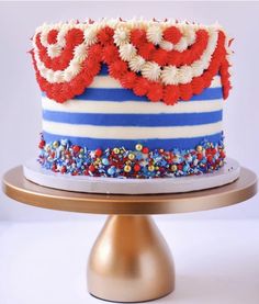 a cake with red, white and blue frosting on a gold plated stand