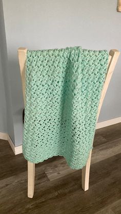 a green crocheted blanket sitting on top of a wooden chair next to a wall