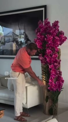 a man placing flowers in a vase on top of a white couch next to a painting