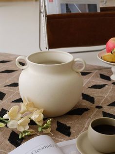 a white vase sitting on top of a table next to a cup and saucer