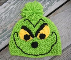 a crocheted green beanie with yellow eyes and a pom - pom