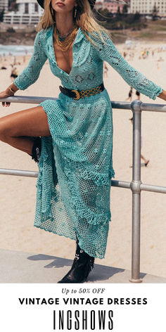 a woman in a blue dress and hat leaning on a rail with her legs crossed