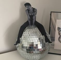 a woman sitting on top of a disco ball with a butterfly in front of her