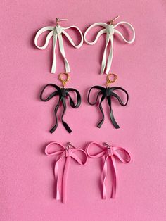 four different colored bows hanging from hooks on a pink surface with gold hardware and black ribbon