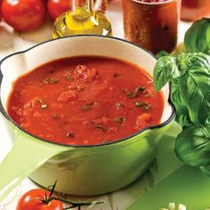 a bowl of tomato soup with basil and tomatoes in the background