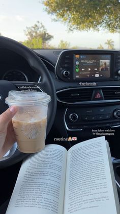 a person holding an open book and a cup of coffee in their hand while driving