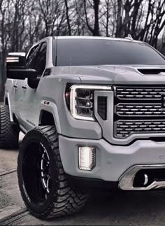 the front end of a silver truck parked on top of a parking lot with trees in the background