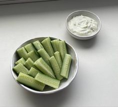 a white bowl filled with cucumber slices next to a small bowl of dip