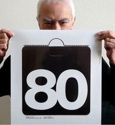 an older man holding up a sign with the number 80 on it in front of his face