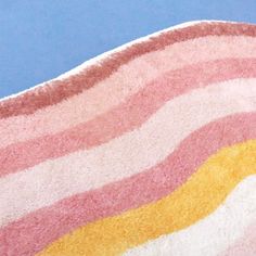 a pink, yellow and white striped rug on a blue background with a cat laying in the middle