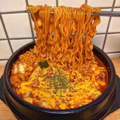 a bowl filled with noodles and sauce on top of a wooden table next to a tiled wall